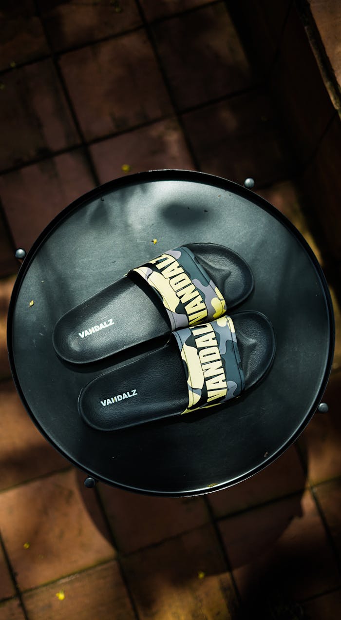 Top view of stylish black camouflage sandals on a round metal table.